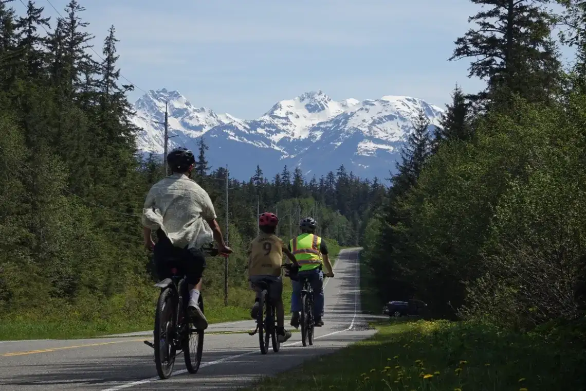 Juneau-rainforest-ebike-mountain-donwhill-tour-1200x800 Group of cyclists on a Juneau bike tour riding towards majestic Alaskan mountains.