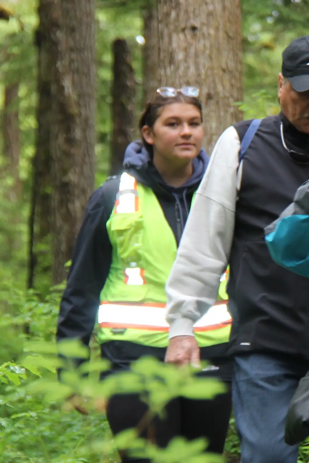 Get to Know Us 12 A young woman in a high-visibility safety vest hikes through a dense forest.