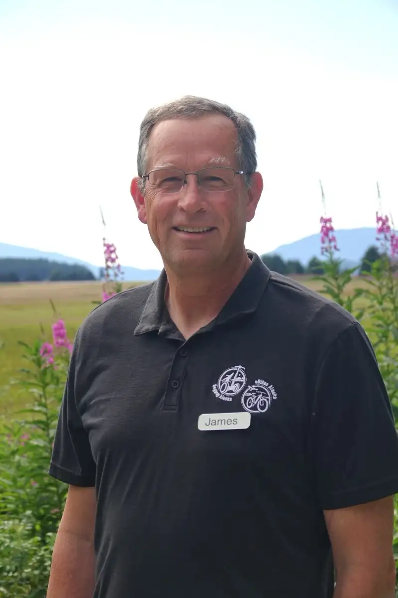 Get to Know Us 2 A smiling man named James wearing glasses and a black polo shirt outdoors.