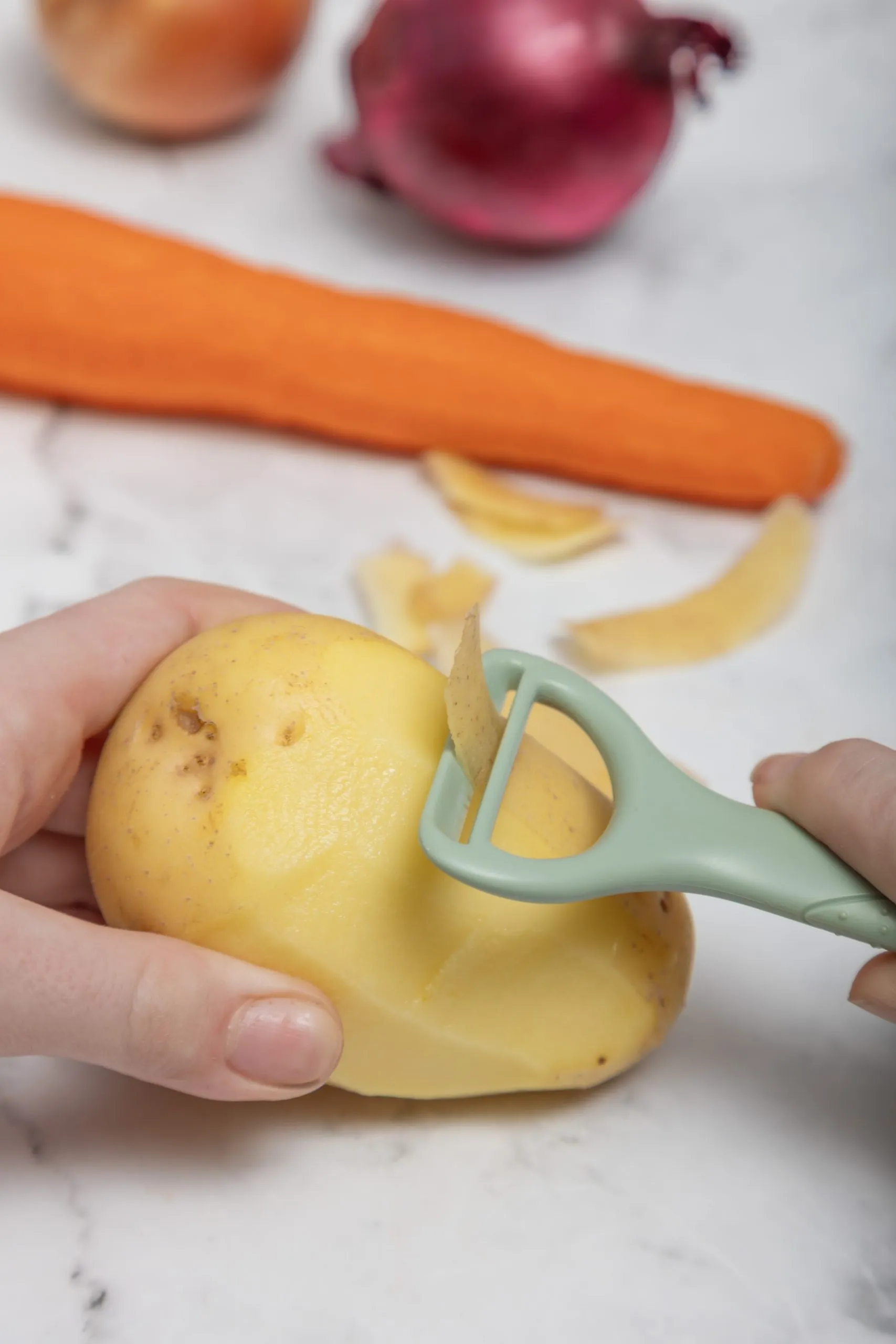 Kiddikutter Safer Peeler with a peeled carrot, tomatoes and cucumber on a kitchen bench
