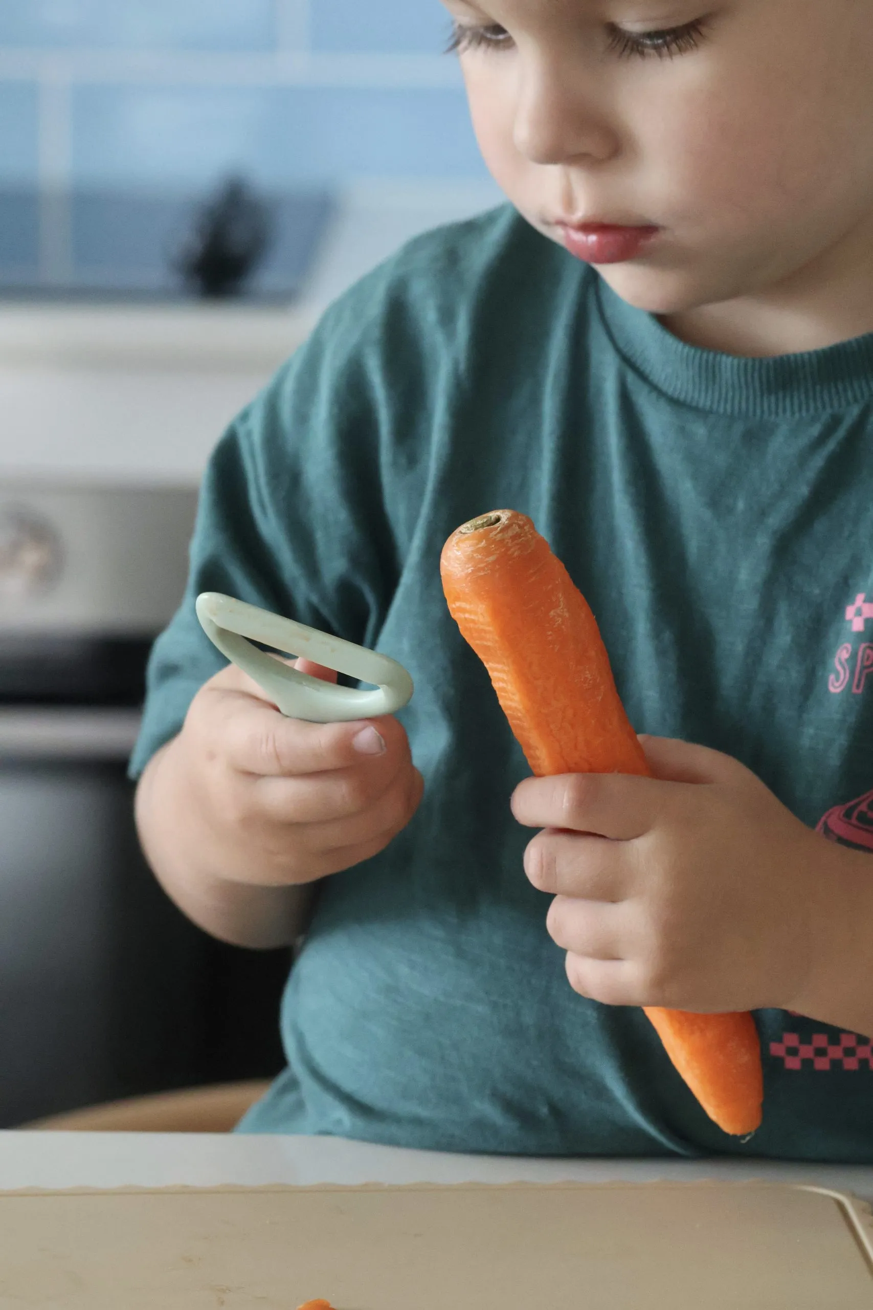 Child holding the KiddiKutter Safer Peeler and a carrot, ready to peel