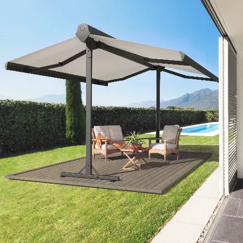 A modern outdoor patio set with two chairs and a table sits on a rug under a large, dual-canopy umbrella beside a backyard pool, with greenery and mountains in the background.