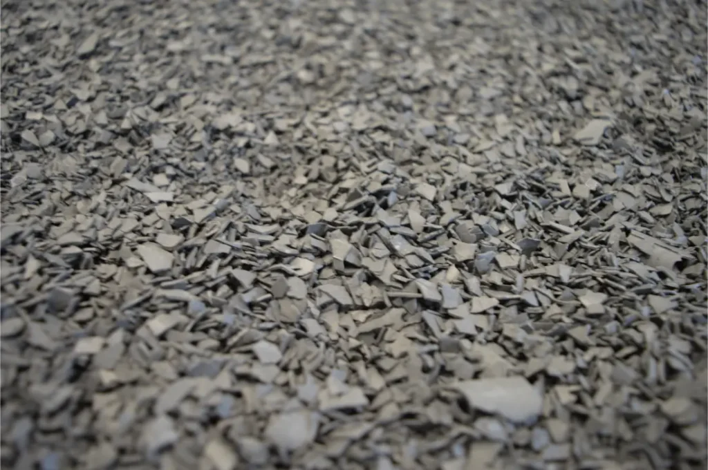 Primer plano de un gran montón de pequeños fragmentos de plástico gris de forma irregular, comúnmente visto como material plástico reciclado utilizado en los neumáticos Schwalbe.