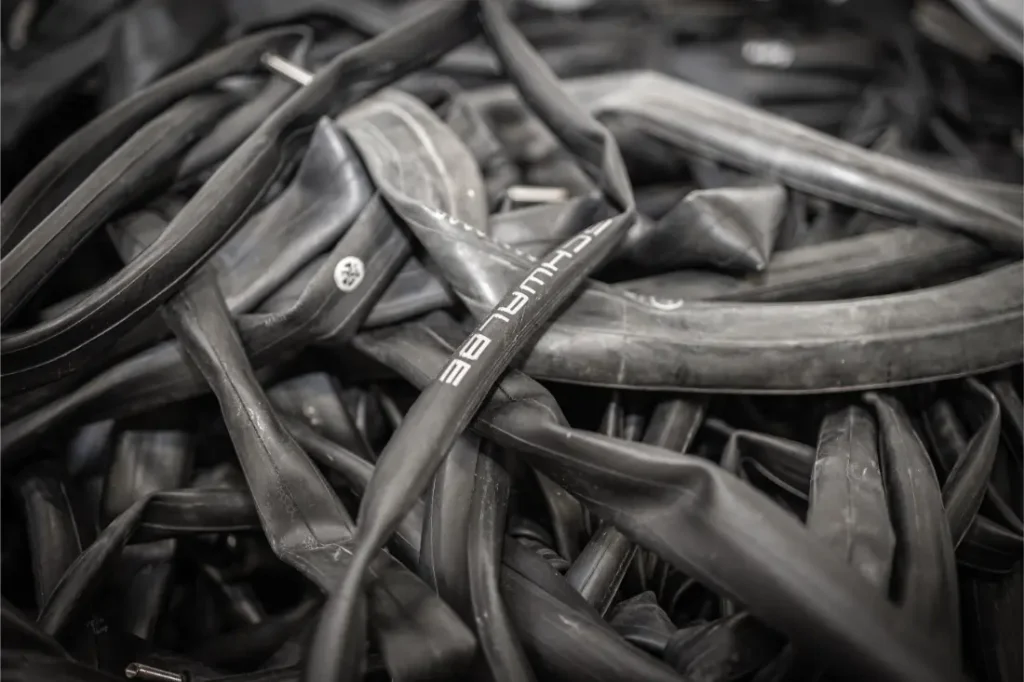 Una pila de cámaras negras usadas de bicicleta, algunas con marcas visibles de la marca Schwalbe, apiladas como neumáticos desechados en un primer plano.