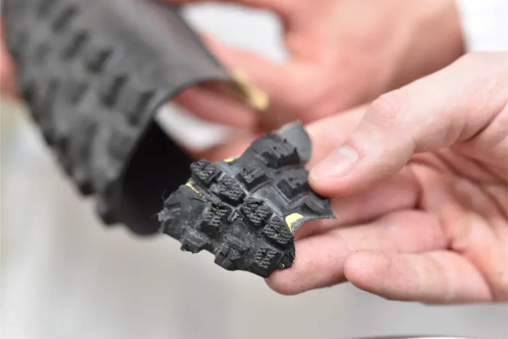 Primer plano de unas manos que sostienen una sección de suela de zapato negra texturizada con dibujos prominentes, que recuerdan a los neumáticos Schwalbe para mejorar el agarre y la durabilidad.
