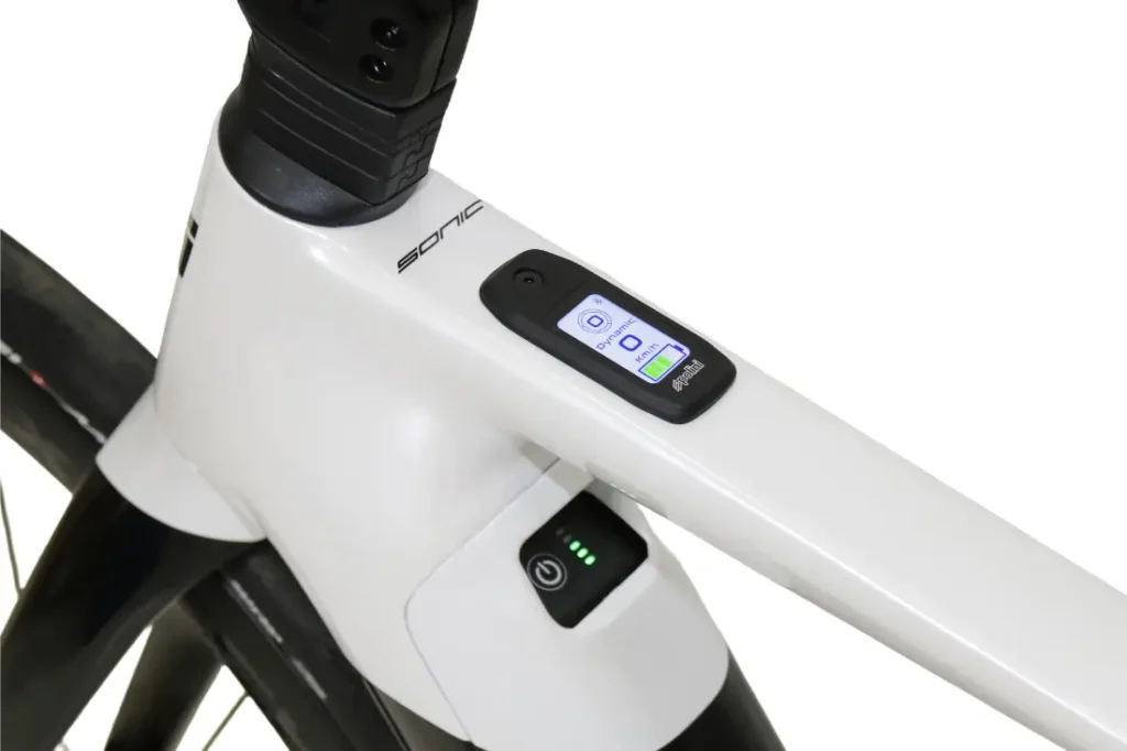 Primer plano del cuadro de una bicicleta blanca en el que se aprecia una pantalla digital integrada y un botón de encendido con luces LED indicadoras.