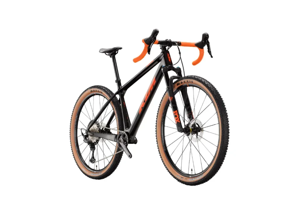 Una bicicleta de gravel negra y naranja con manillar de carretera y neumáticos de flanco marrón claro, representada sobre un fondo blanco.