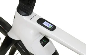 Primer plano del cuadro de una bicicleta blanca en el que se aprecia una pantalla digital integrada y un botón de encendido con luces LED indicadoras.