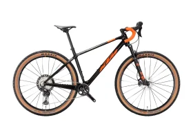 Se muestra una bicicleta de montaña negra y naranja, con manillar curvo y neumáticos de flanco marrón claro, en una vista lateral sobre un fondo blanco.