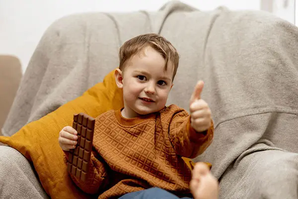 Boy Sitting On Sofa Eating Mr Popples Chocolate Bar With Thumbs Up