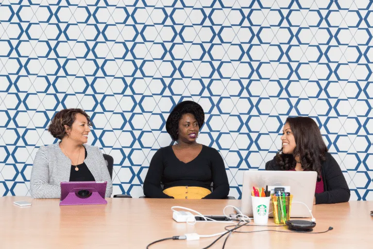 diversiteit HR werkvloer Vivian Acquah inclusie Three women having a discussion at a conference table with a geometric blue and white background