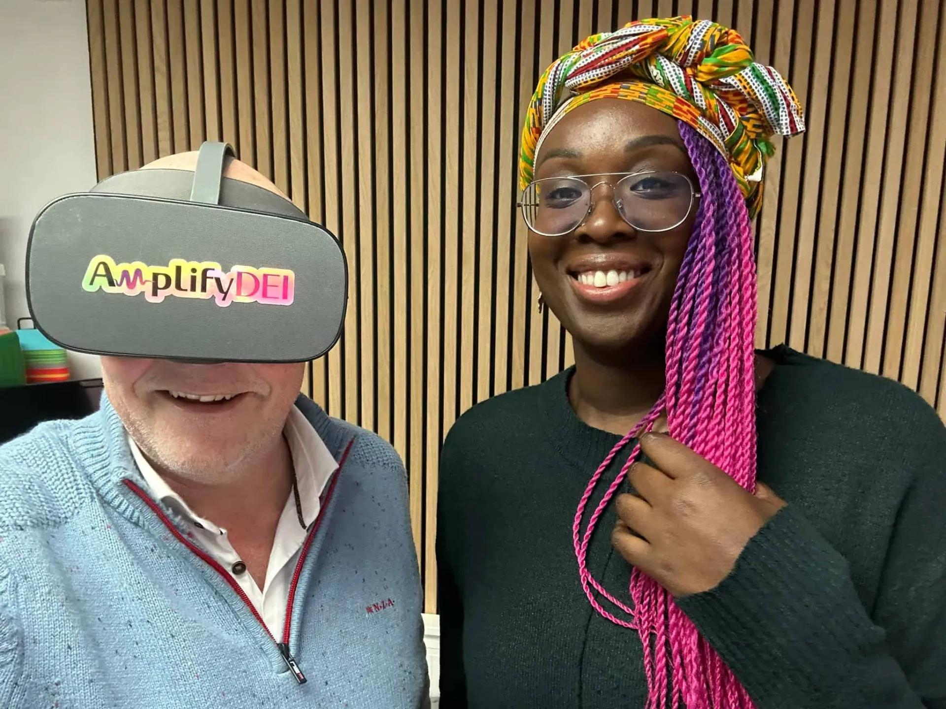 De essentie van leren vivian acquah arco kats training VR virtual reality leiderschap Two people smiling; one wearing a VR headset with 'Amplify DEI' on it, and the other with colorful braids and a headwrap