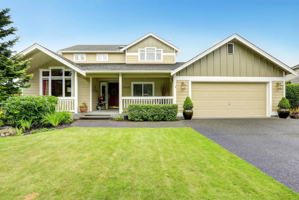 Une maison à deux étages avec une pelouse verte nécessitant un entretien de pelouse à Lavaur, un extérieur beige, des boiseries blanches, un porche et un garage pour deux voitures.
