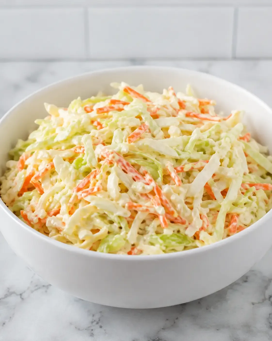 Creamy classic coleslaw with shredded green cabbage and carrots in a white bowl.