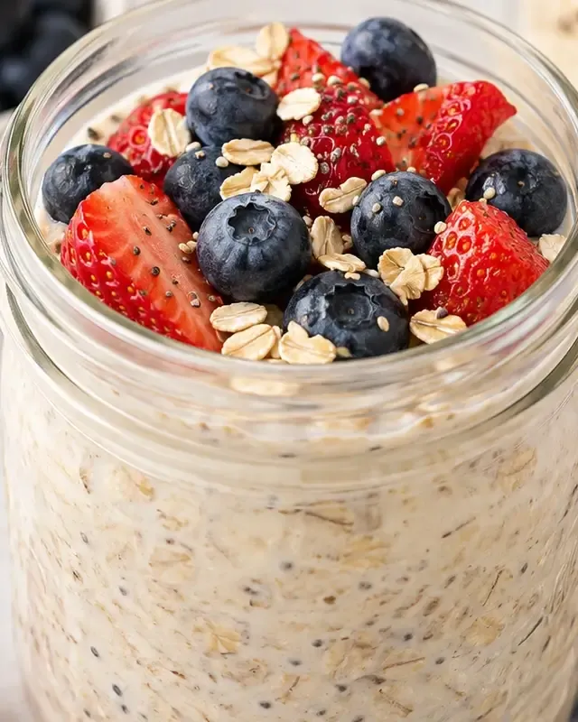 Creamy overnight oats topped with strawberries and blueberries in a clear glass jar.