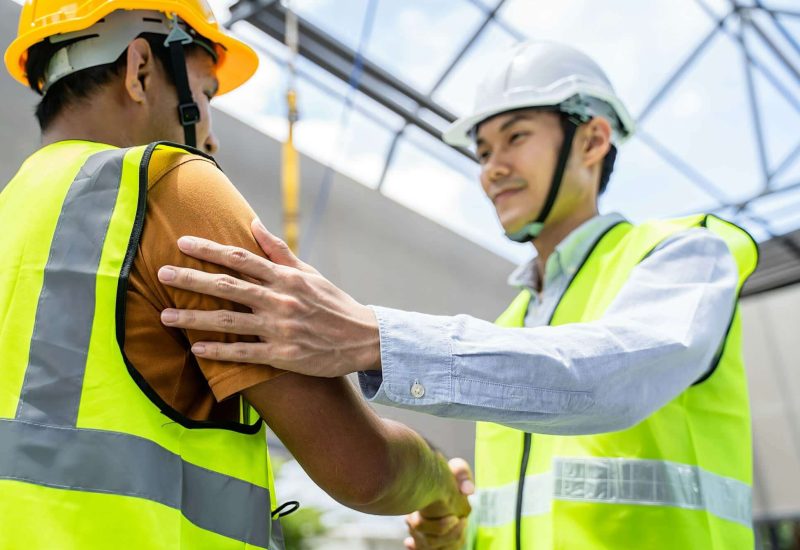 Asian structure engineer and worker making handshake on building working site.
