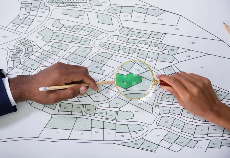 Human Hand Holding Magnifying Glass Over Cadastre Map