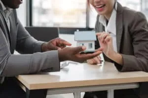 Agents and clients discuss contracts to buy, insure, or borrow real estate or assets. along with viewing a sample house model.
