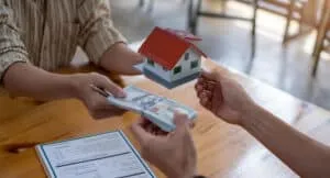 business people handing over dollars with decorative house model and contract at office