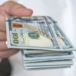 A person in a white shirt holds out a stack of U.S. hundred-dollar bills, symbolizing the cash flexibility often discussed in Hard Money vs Traditional Loans.