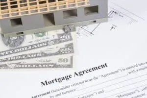 Model house with US dollar bills placed on top of a mortgage agreement document.