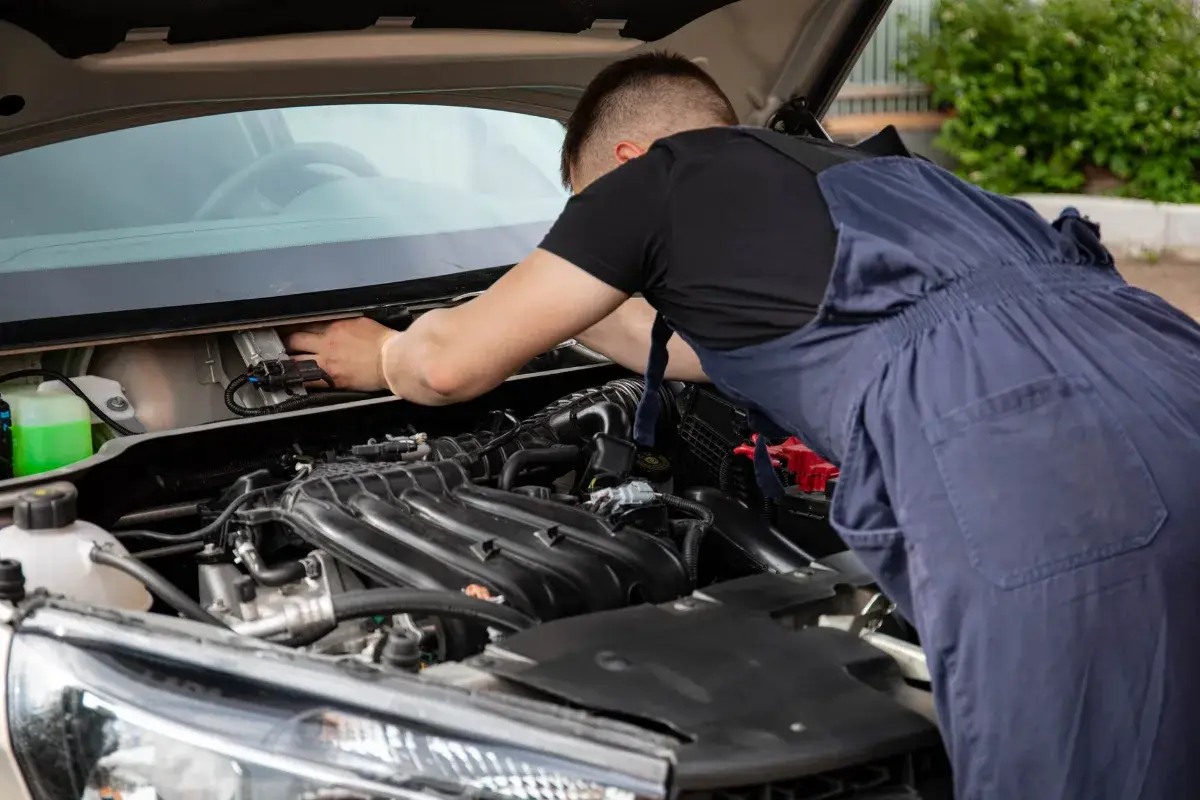 A mechanic performing maintenance work on a car's engine in an outdoor setting