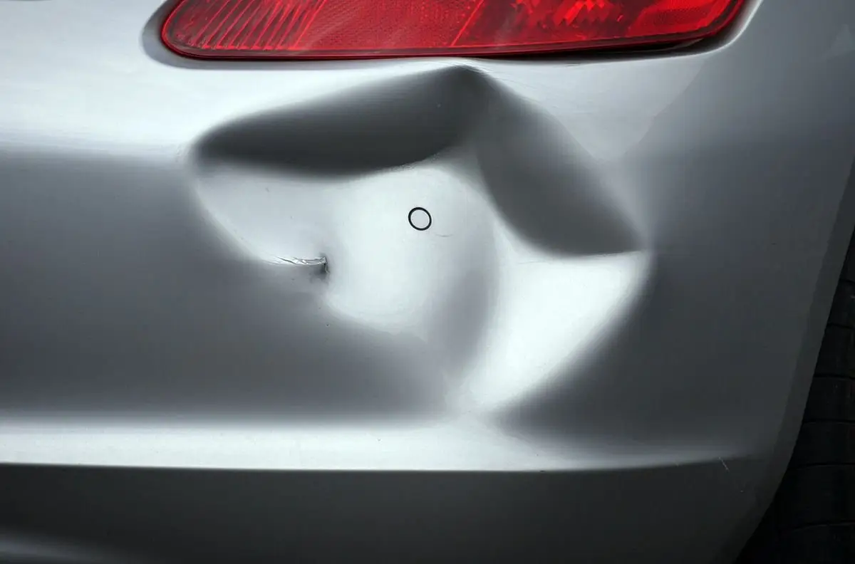 Close-up of a large dent in a silver car bumper below the tail light, a candidate for dent repair
