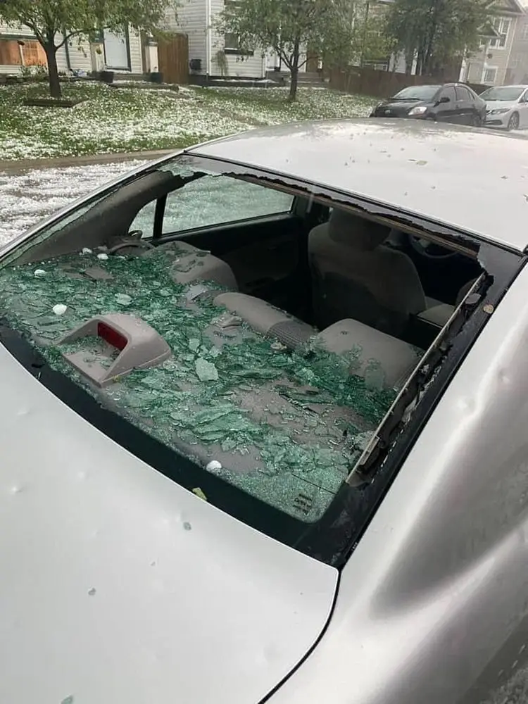 Silver car with a smashed rear window and hailstones on the trunk after a hailstorm, showing hail damage car repair needs