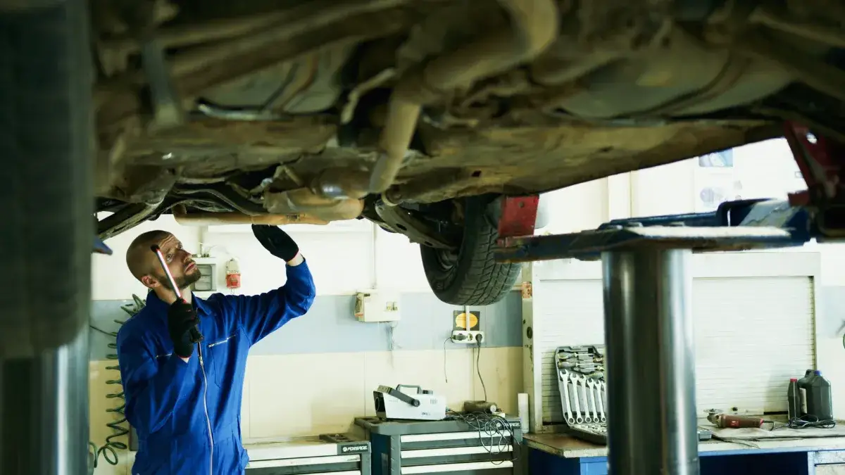 Mechanic inspecting a car's underside in a workshop for repairs