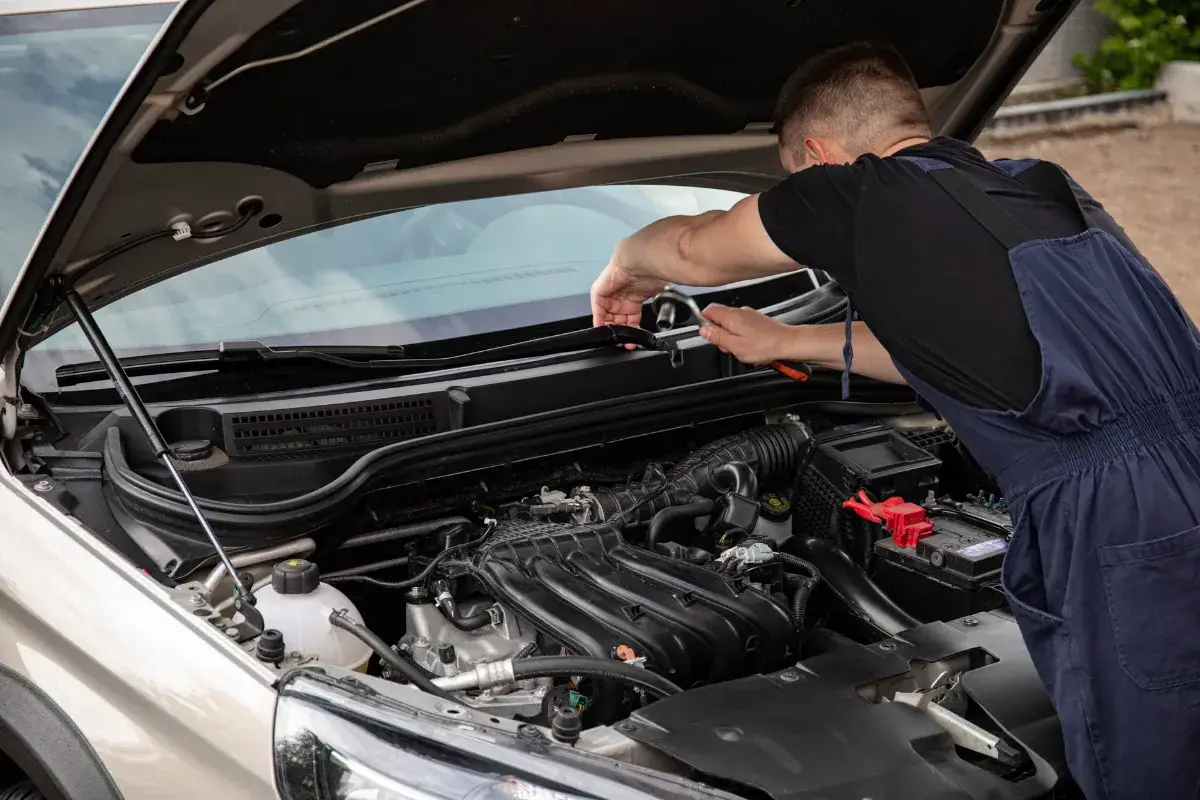 A mechanic uses tools to repair a car engine outdoors in daylight