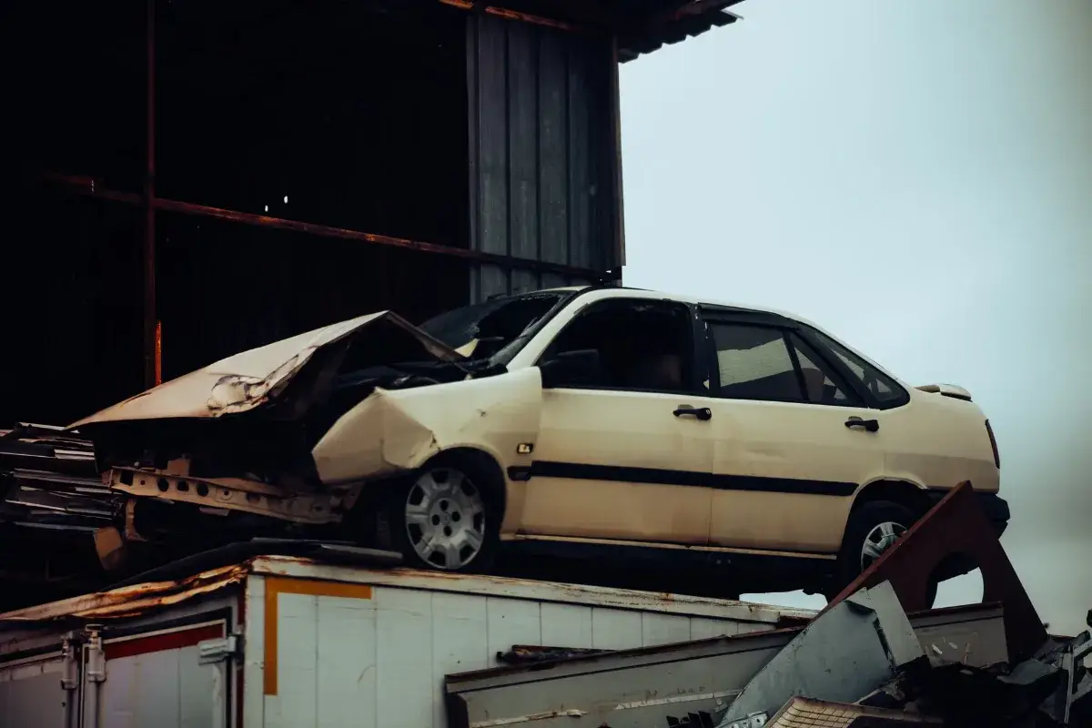 A damaged car sits atop a metal scrap heap, showing a scene of automotive decay