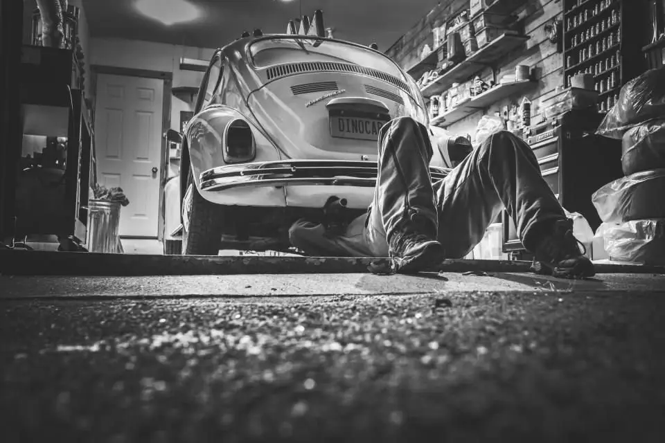 Mechanic lying under a classic car in a garage during a pre-purchase inspection of a used car