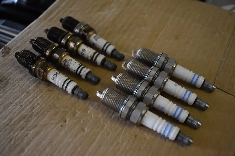 Old and new spark plugs laid out side by side before a spark plug replacement