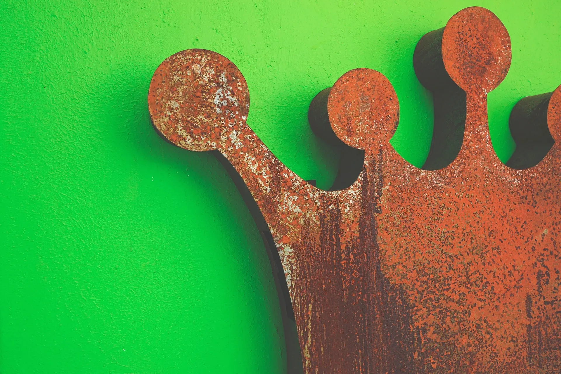Eine Nahaufnahme einer verrosteten Metallkronenskulptur vor einer leuchtend grün gestrichenen Wand, die durch ihre dauerhafte Stärke und ihren einzigartigen Charakter ein gesundes Selbstwertgefühl symbolisiert.