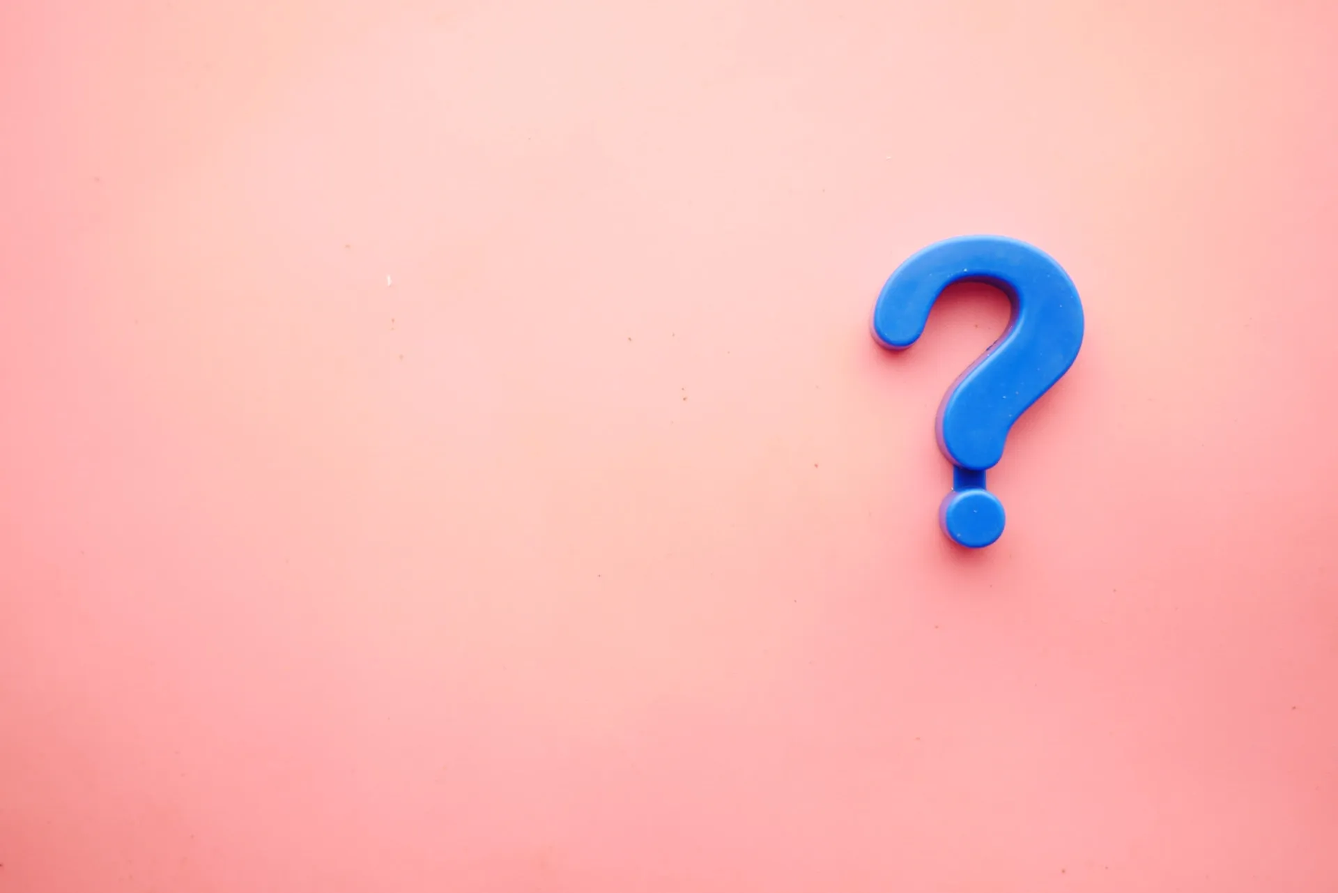 In der rechten Bildhälfte befindet sich ein blaues Fragezeichen aus Kunststoff, das die systemische beratung symbolisiert, auf einem einfarbigen rosa Hintergrund.