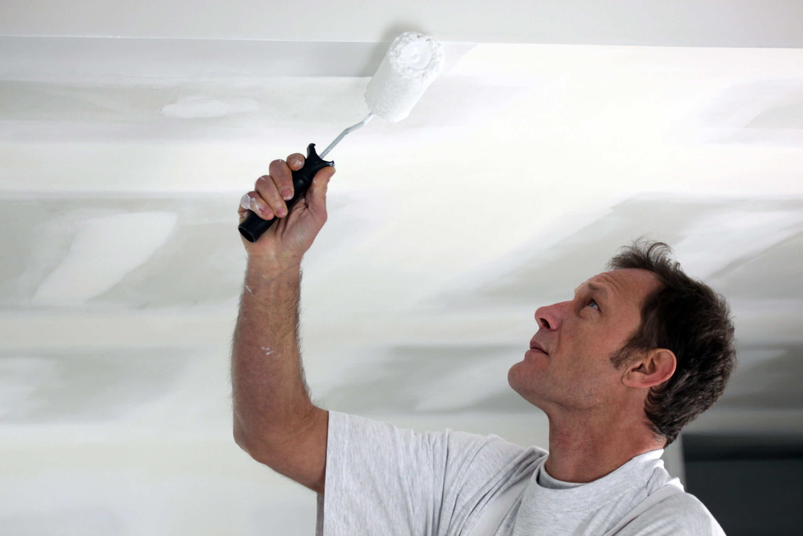 A painter is painting the ceiling in white colour