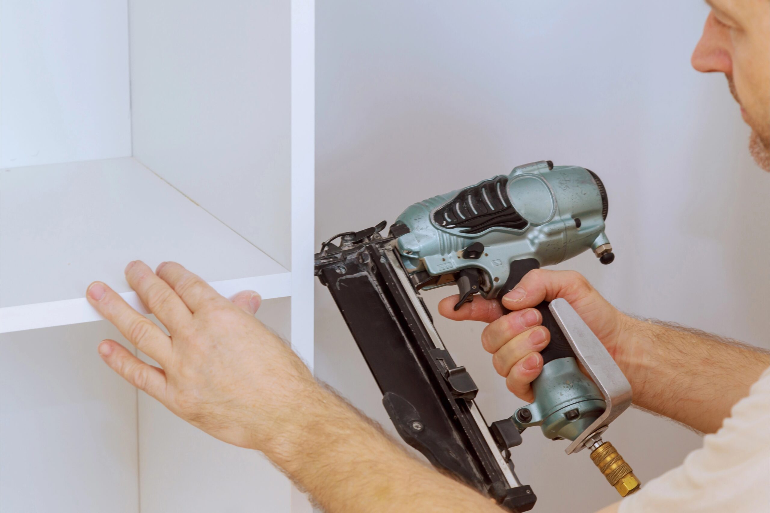 TJ Handyman Services installer using a nail gun to secure a white shelving unit during a shelving installation project in Orlando, FL.