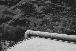 Close-up of a corroded metal pipe and rivets on a weathered surface, reminiscent of the rugged craftsmanship seen in custom magnetic drive pump solutions, with a blurred background of rocky hills. Black and white image.