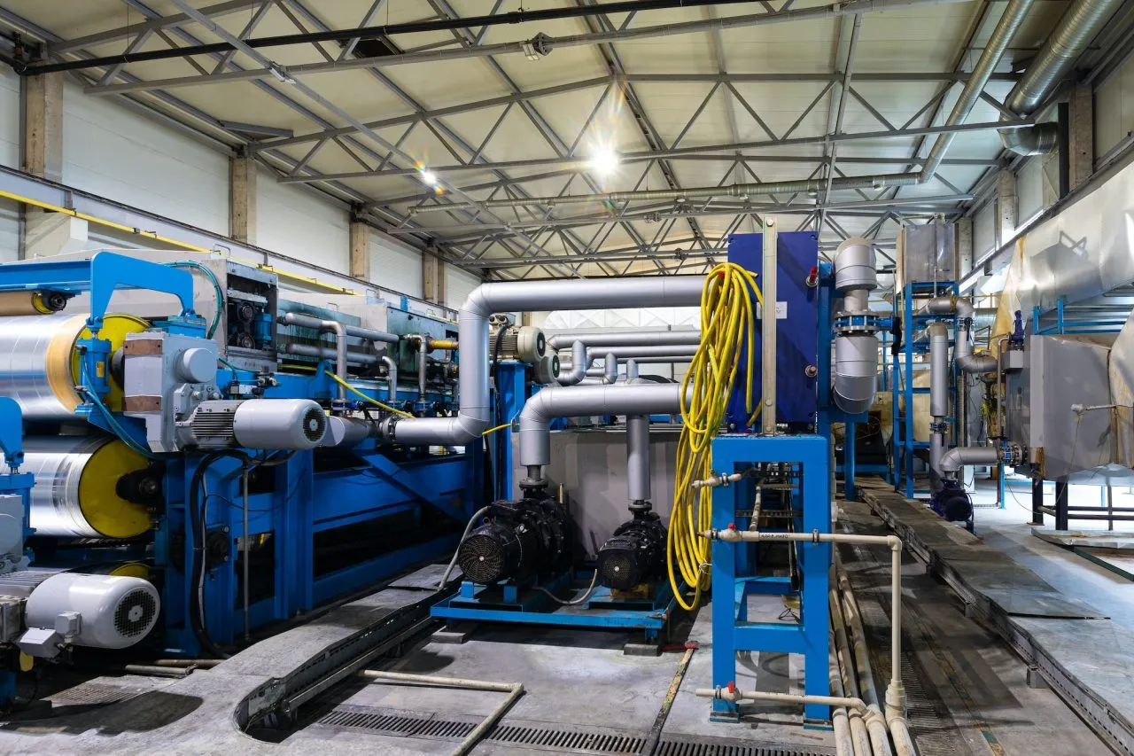 Industrial machinery with large pipes, blue framework, and yellow cables sits in a factory setting, highlighted by exposed beams and lights overhead. Reliable centrifugal pump suppliers are integral to this efficient operation.