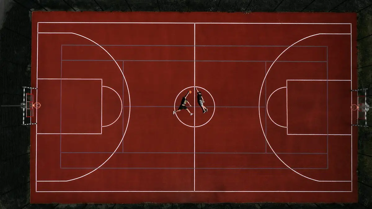 Aerial view of a red outdoor basketball court with two players lying at center court