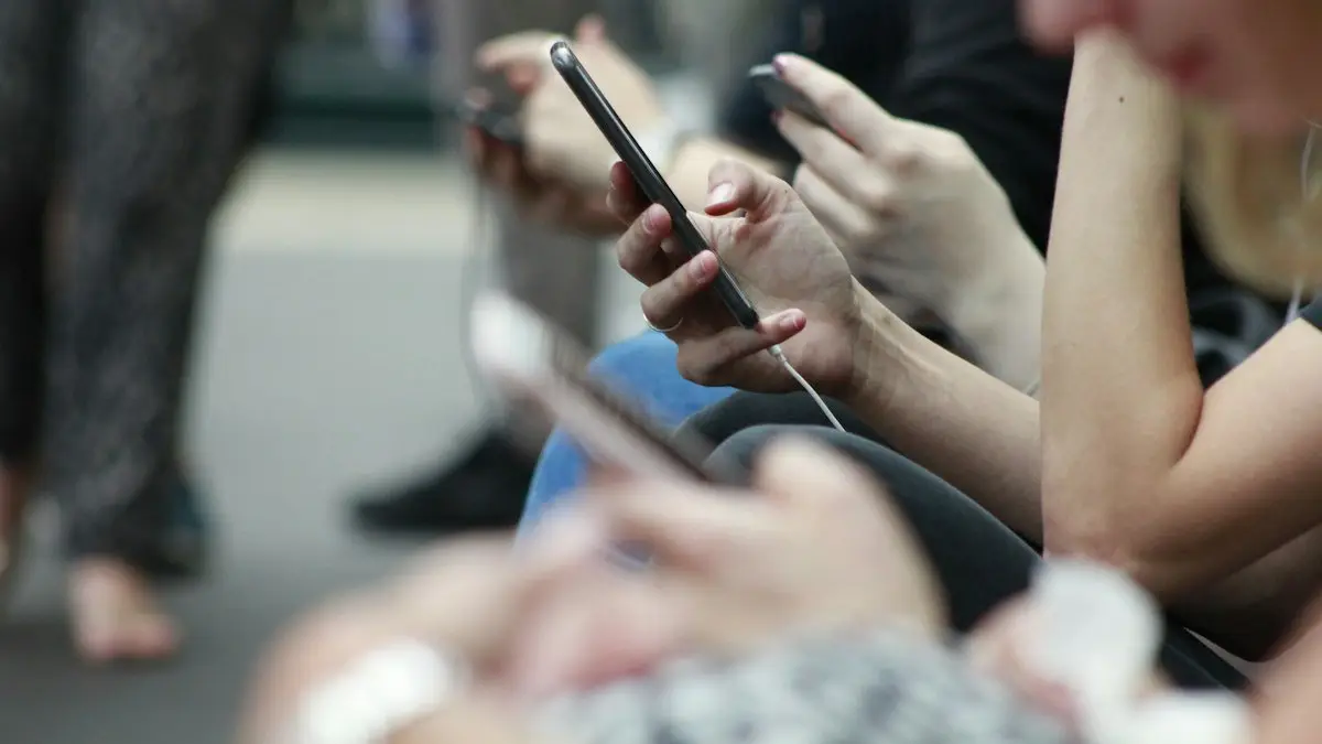 Hands holding smartphones as seated commuters scroll through their screens