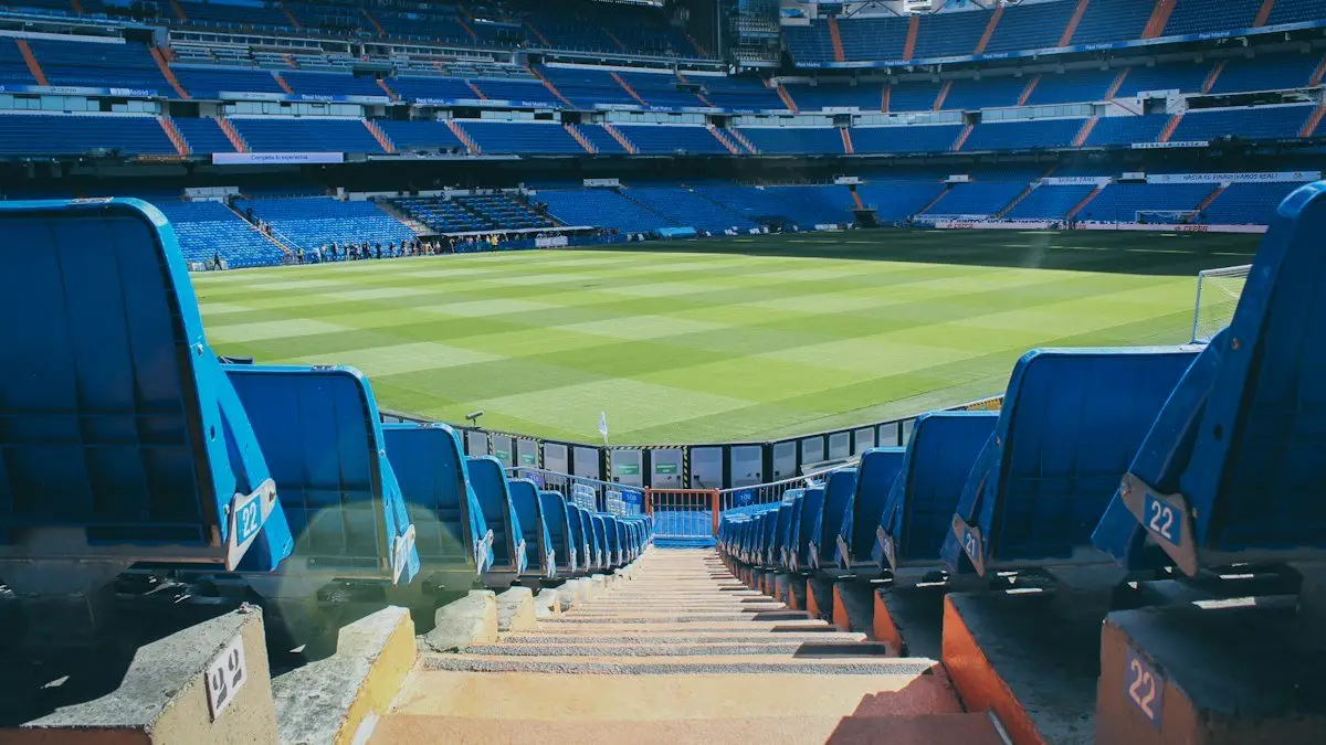 Rows of empty blue seats and concrete steps looking out over the pitch of a large football stadium