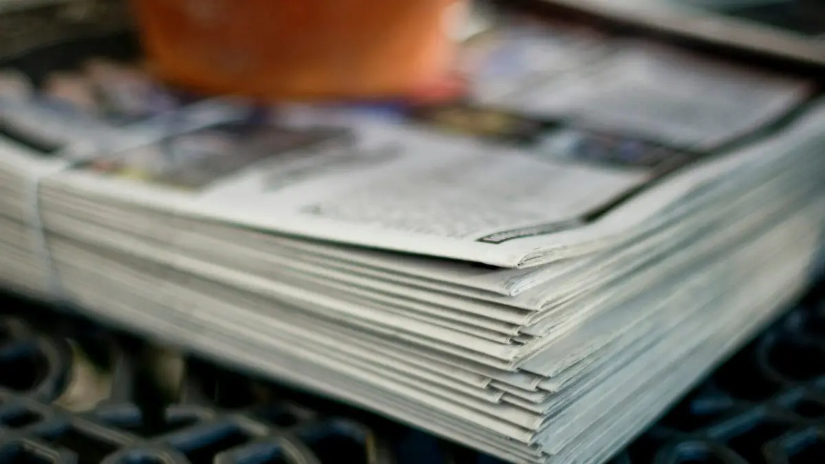 A stack of folded newspapers resting on a dark metal grate