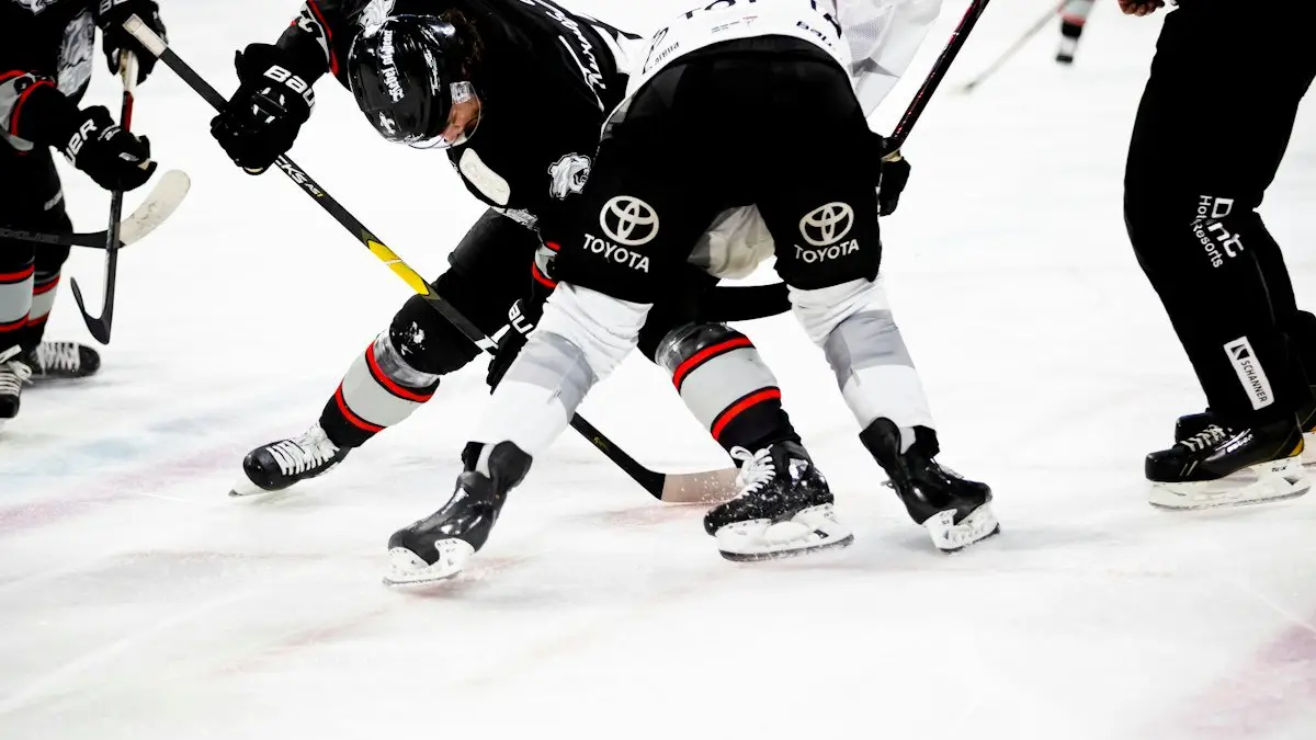 Two hockey players bent over at a faceoff on the ice, with sticks down and a referee standing nearby