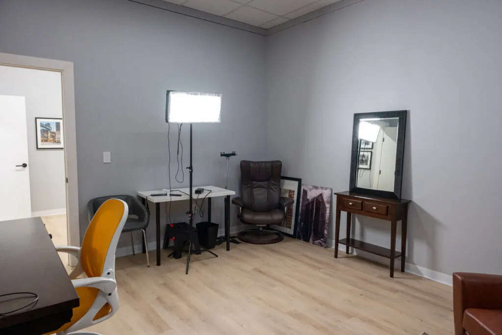 Soundproofed Houston podcast and video interview studio with LED panel light, leather recliner, floor mirror, and ergonomic chairs on light hardwood flooring.