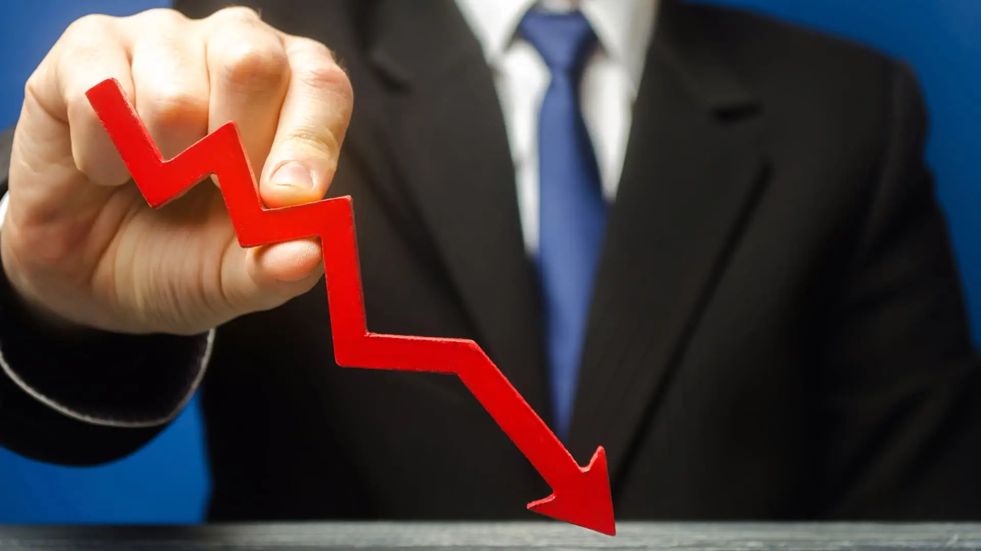 Businessperson holding a red downward arrow representing declining performance