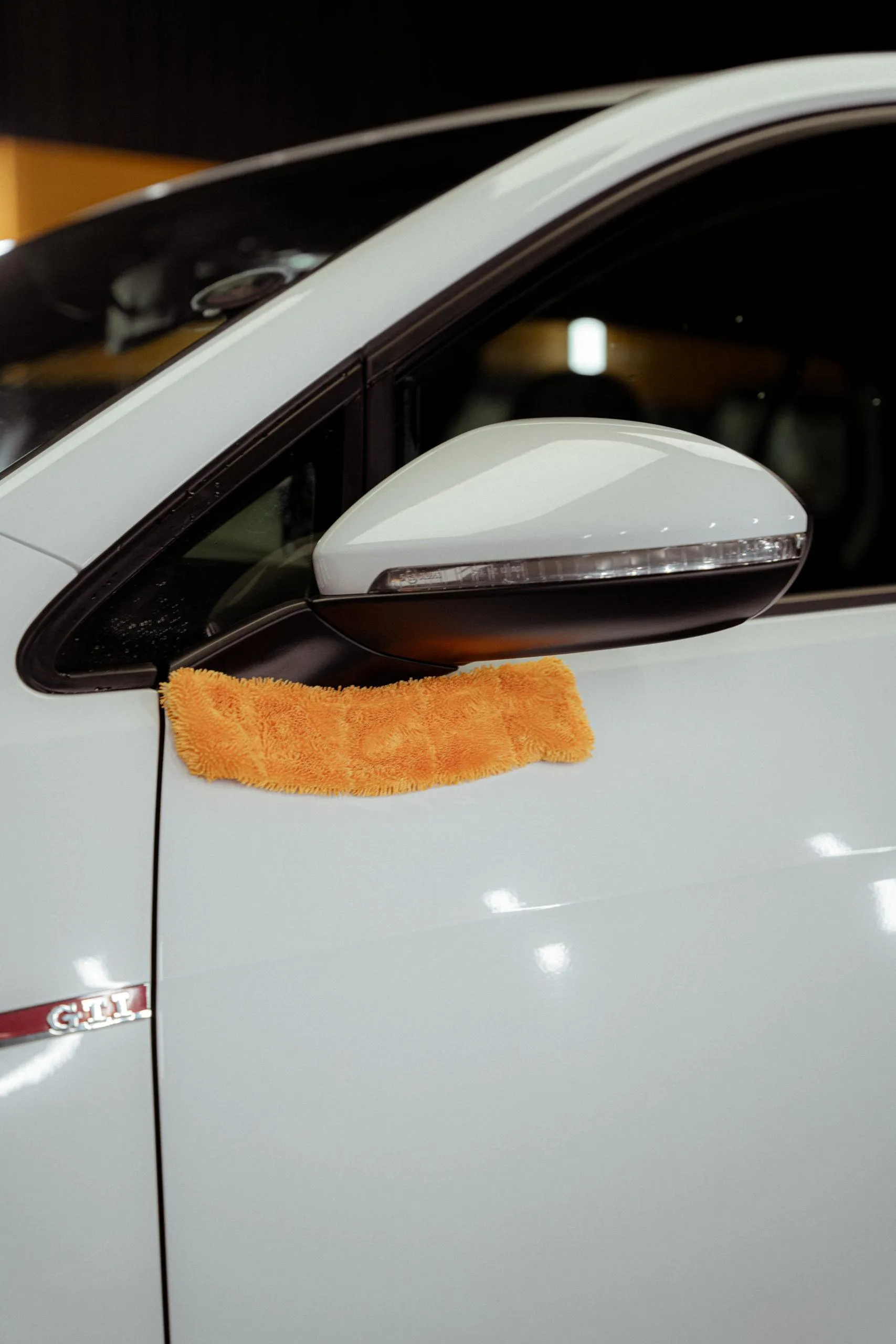 Close-up of a white car's side mirror with an orange microfiber towel draped over it, ready for detailing.
