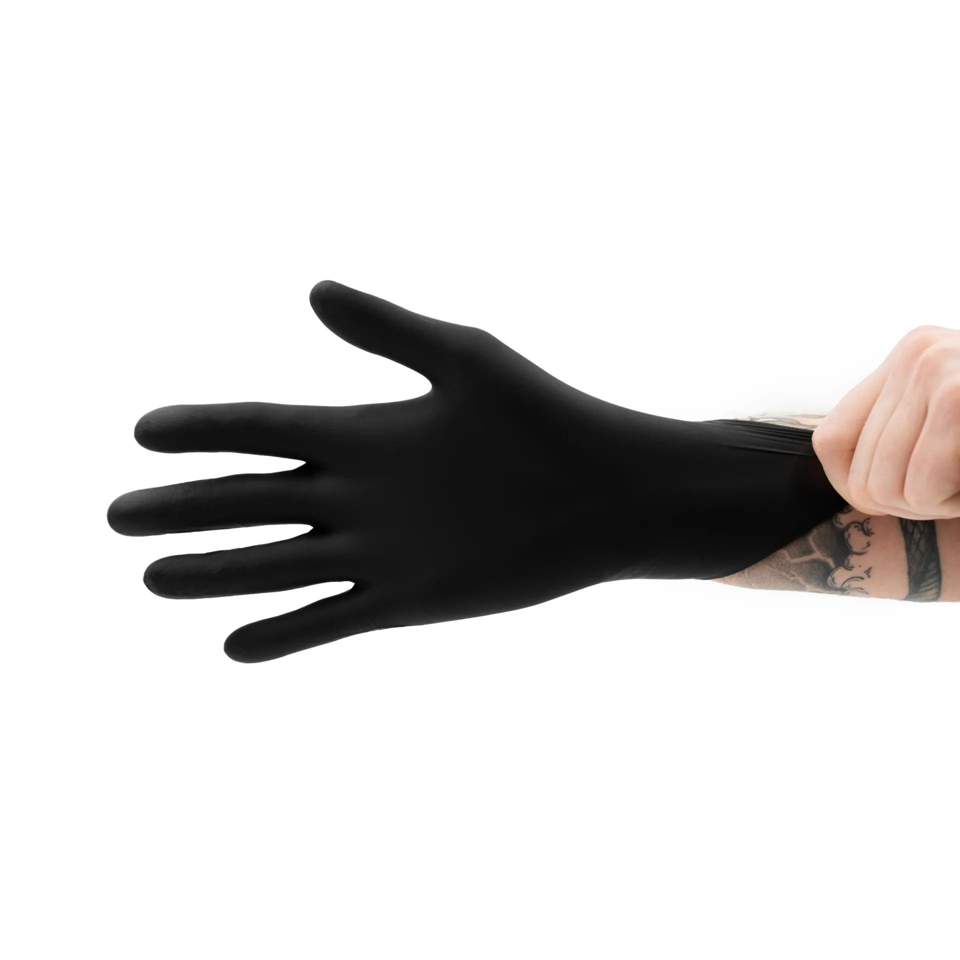 Un brazo tatuado extiende sobre la mano un guante negro desechable sobre un fondo blanco liso.