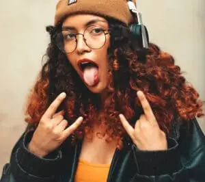 jeune femme aux cheveux bouclés tirant la langue et faisant des signes rock n' roll avec ses mains