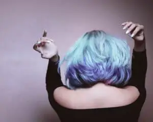 Femme aux cheveux mi-longs colorés en couleurs pastelles et gris, de dos, avec les bras en l'ai pour montrer sa coloration cheveux